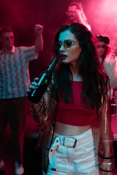 Hermosa chica en gafas de sol beber cerveza en discoteca durante rave - foto de stock