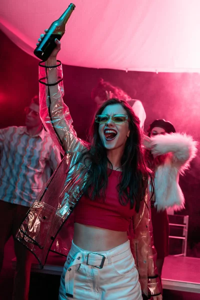 Excitado chica con botella de alcohol durante rave en discoteca - foto de stock