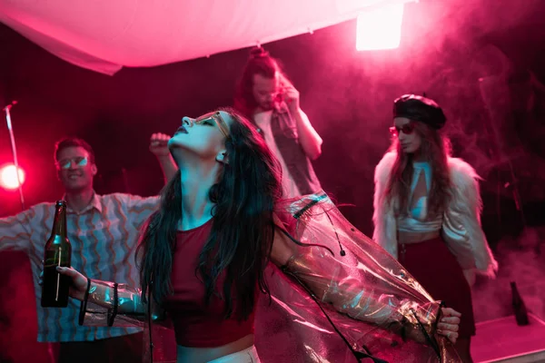 Девушка держит пиво и танцует в ночном клубе с розовым дымом — стоковое фото