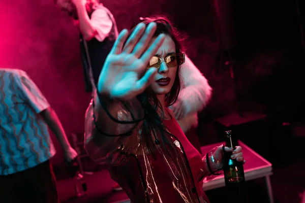 Girl Gesturing with hand and holding bottle of alcohol during rave in nightclub — Stock Photo