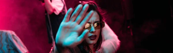 Panoramic shot of girl in sunglasses showing hand at camera in nightclub during rave party — Stock Photo