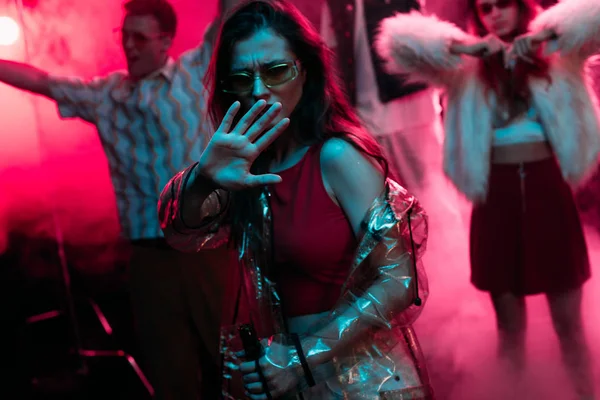 Дівчина жестикулює рукою під час танців у нічному клубі з рожевим димом — стокове фото