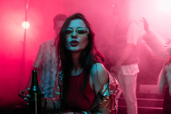 Hermosa chica sosteniendo cerveza en discoteca y bailando durante rave — Stock Photo