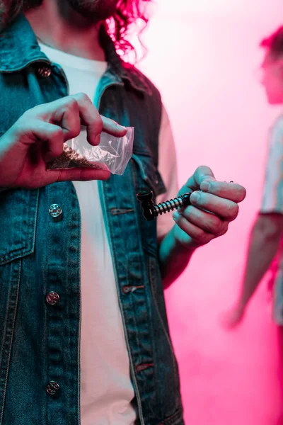 Vista recortada del hombre poniendo marihuana en pipa de fumar en discoteca - foto de stock