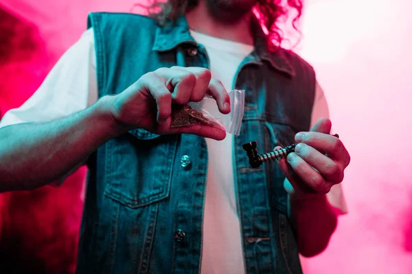 Vista recortada del hombre poniendo marihuana en pipa de fumar en discoteca - foto de stock