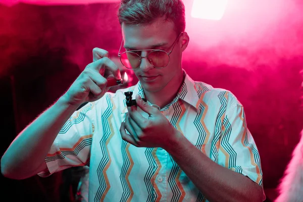 Hombre guapo iluminación pipa de fumar con marihuana en discoteca - foto de stock