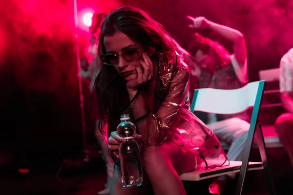 Sick young woman sitting with bottle of water in nightclub — Stock Photo