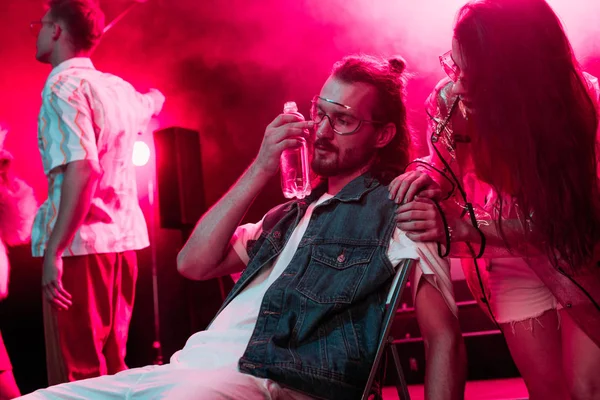 Chica mirando enfermo hombre sentado con botella de agua en nightclub - foto de stock