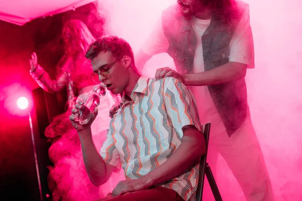 Hombre chequeando enfermo hombre sentado con botella de agua en discoteca - foto de stock