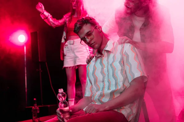 Man checking on sick man sitting with bottle of water in nightclub — Stock Photo