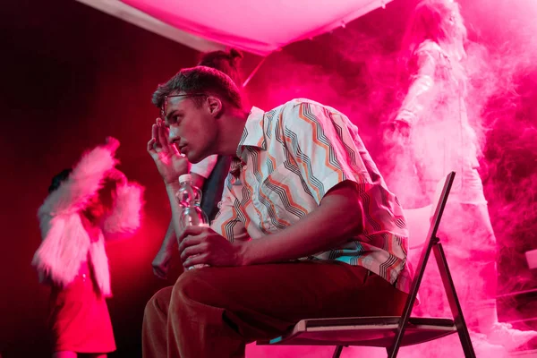 Man sitting with bottle of water in nightclub and touching head — Stock Photo