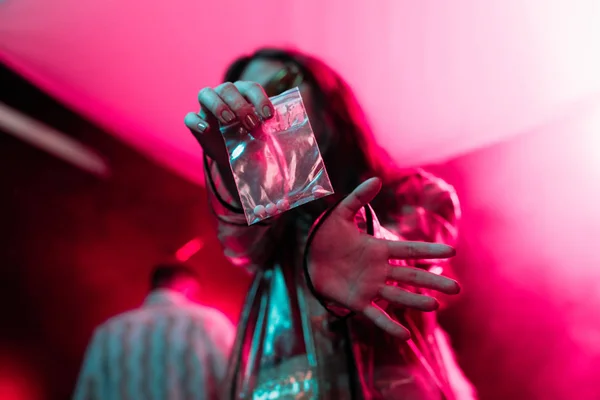 Girl holding plastic zipper bag with drugs in nightclub, selective focus — Stock Photo