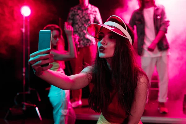 Girl pouting lips and taking selfie on smartphone during rave party in nightclub — Stock Photo