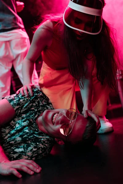 Chica ayudando hombre enfermo acostado en el suelo en discoteca - foto de stock