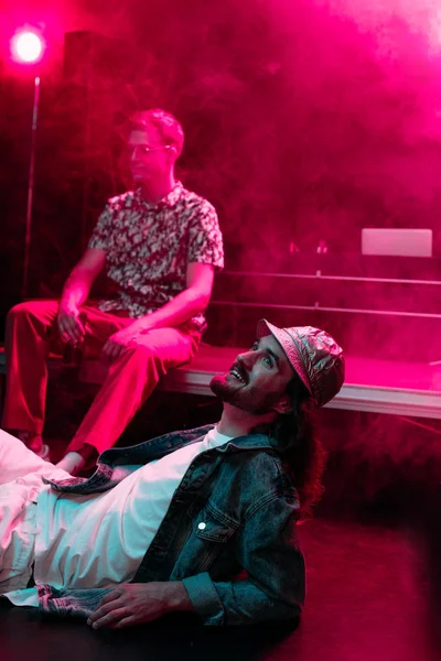 Усміхнений чоловік лежить на підлозі в нічному клубі під час вечірки з рожевим димом — стокове фото