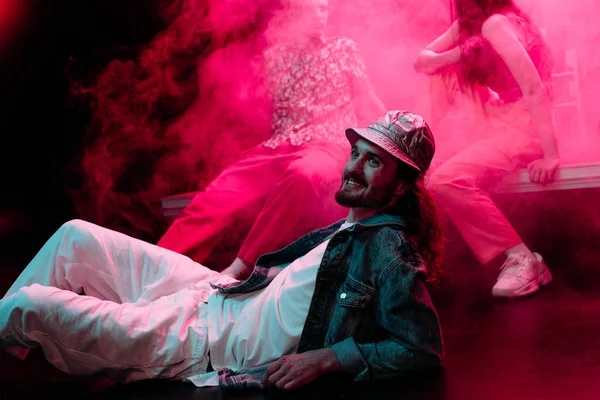 Smiling man lying on floor in nightclub during rave party with pink smoke — Stock Photo