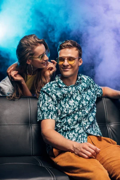 Homme assis sur le canapé près de la jeune femme pendant la fête de rave dans la boîte de nuit — Photo de stock