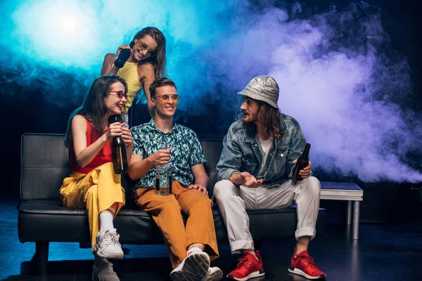 Happy young women and men with alcohol sitting on couch in nightclub — Stock Photo