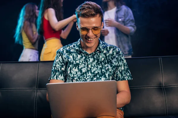 Mann mit Sonnenbrille sitzt auf Couch und benutzt Laptop in Nachtclub — Stockfoto