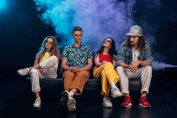 Men and young women in sunglasses sitting on couch in nightclub during rave party — Stock Photo