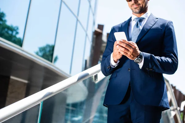 Vista ritagliata dell'uomo in giacca e cravatta utilizzando lo smartphone esterno — Foto stock