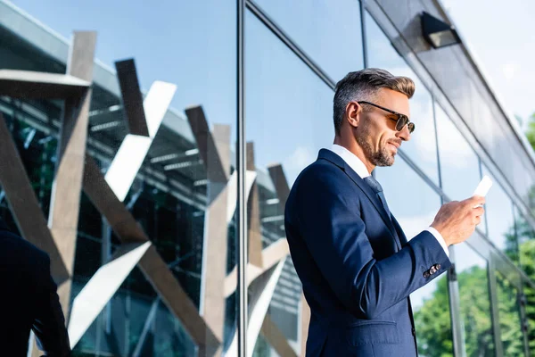 Seitenansicht eines gutaussehenden Mannes in Anzug und Brille mit Smartphone — Stockfoto