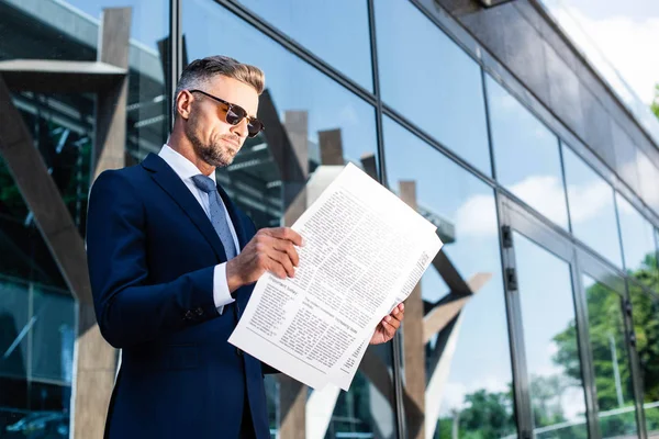 Schöner Mann in Anzug und Brille, der draußen Zeitung liest — Stockfoto