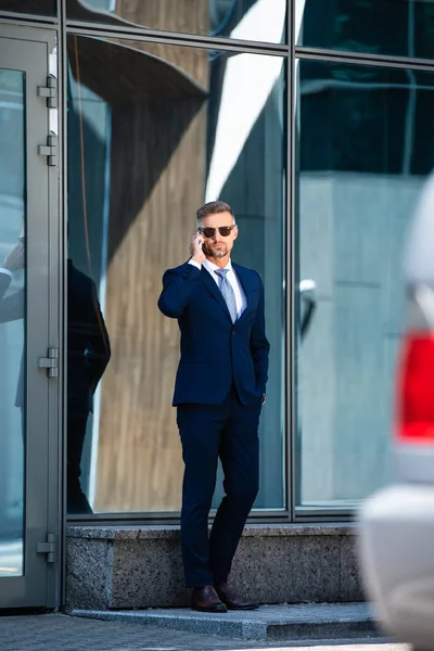 Schöner Mann in Anzug und Brille mit Hand in Tasche, der auf dem Smartphone spricht — Stockfoto