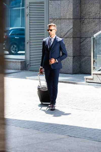 Schöner Mann in Anzug und Brille mit Koffer und Blick — Stockfoto