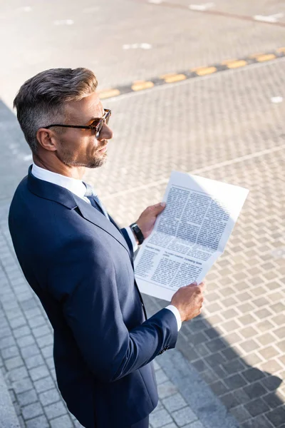 Vista de ángulo alto del empresario sosteniendo periódico y mirando hacia otro lado - foto de stock