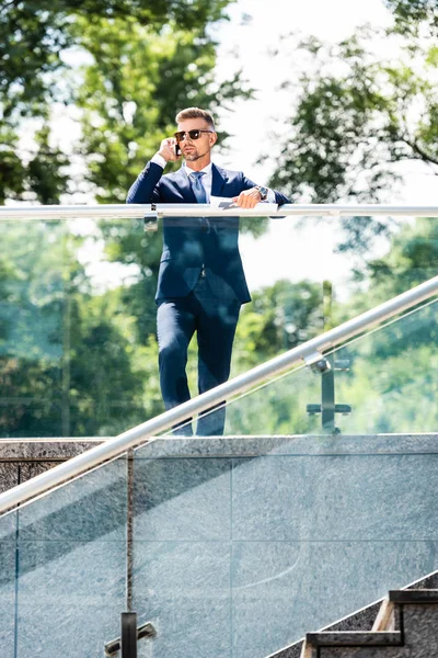 Hombre de negocios guapo en traje y gafas hablando en smartphone - foto de stock