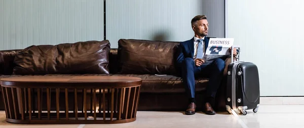 Plano panorámico de hombre de negocios guapo en traje celebración de periódico - foto de stock