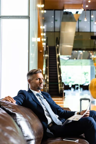 Schöner Geschäftsmann im Anzug sitzt auf dem Sofa und hält Zeitung — Stockfoto