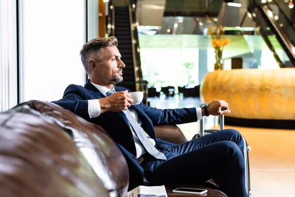 Vista lateral del hombre de negocios guapo en traje sosteniendo taza - foto de stock