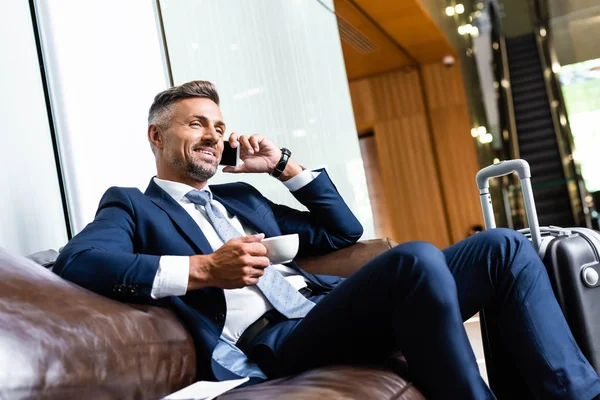 Schöner Geschäftsmann im Anzug, der mit Smartphone und Becher spricht — Stockfoto