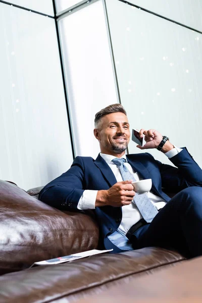 Bel homme d'affaires en costume parlant sur smartphone et tenant tasse — Photo de stock