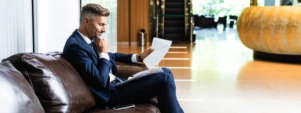 Plano panorámico de hombre de negocios guapo en traje mirando los papeles - foto de stock