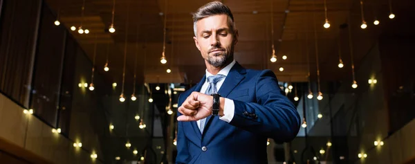 Tiro panorâmico de homem de negócios em terno olhando para relógio — Fotografia de Stock