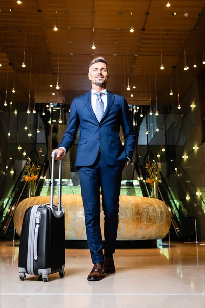 Homem de negócios bonito em terno com mão no bolso segurando mala — Fotografia de Stock