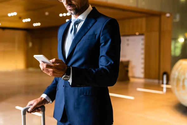 Vista recortada del hombre de negocios en traje usando teléfono inteligente en el hotel - foto de stock