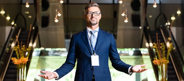 Tiro panorâmico de empresário bonito em terno e óculos com as mãos estendidas — Fotografia de Stock