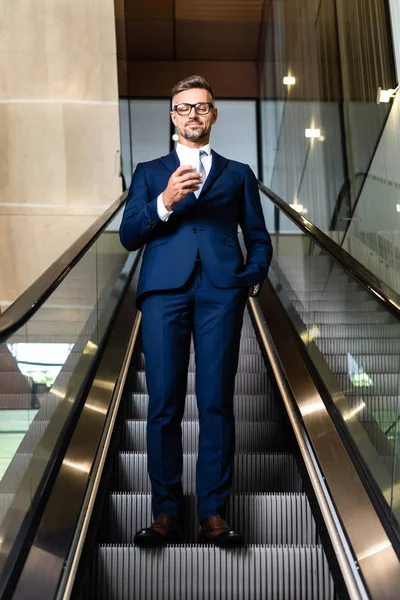 Homem de negócios bonito em terno e óculos com mão no bolso usando smartphone — Fotografia de Stock