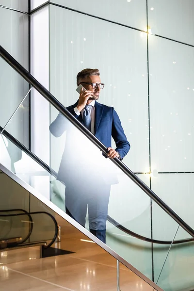 Handsome businessman in suit and glasses talking on smartphone — Stock Photo