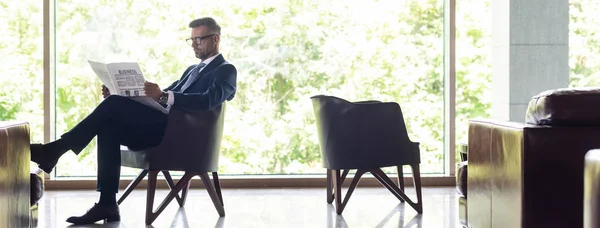 Tiro panorâmico de empresário bonito no jornal de leitura de terno — Fotografia de Stock