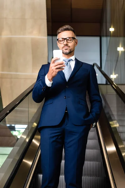 Hombre de negocios guapo en traje y gafas hablando en smartphone - foto de stock