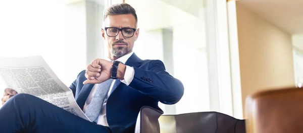 Tiro panorâmico de empresário bonito em terno e óculos olhando para relógio — Fotografia de Stock