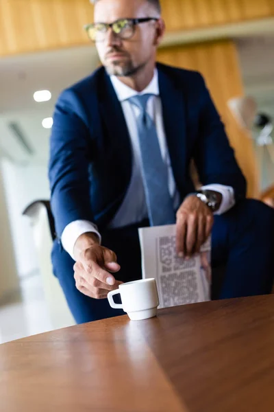 Selective focus of handsome businessman in suit and glasses taking cup — Stock Photo