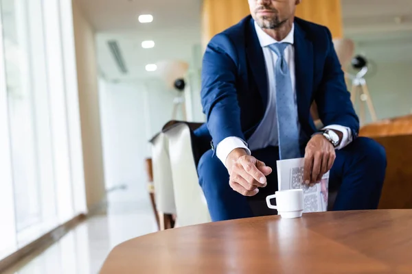 Recortado vista de hombre de negocios en traje tomando taza y sosteniendo periódico - foto de stock