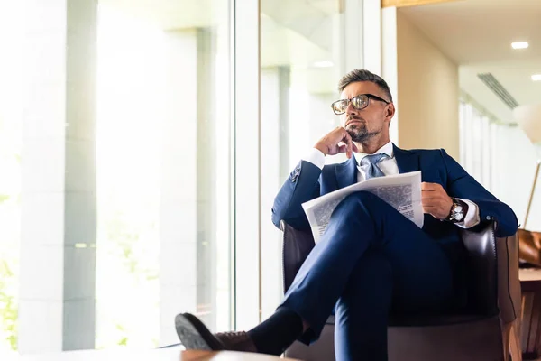 Bel homme d'affaires en costume et lunettes tenant le journal et détournant les yeux — Photo de stock