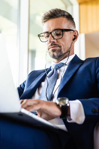 Handsome businessman in suit and glasses with earphones using laptop — Stock Photo